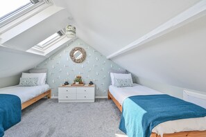 A cozy attic bedroom with two beds, a dresser, and a skylight.