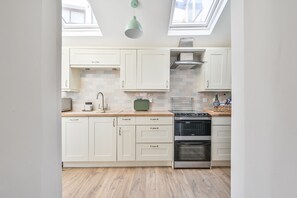 A modern kitchen with white cabinets, a wooden countertop, a green hanging light, and a stainless steel oven.
