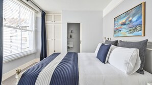 Ein Schlafzimmer mit einem großen Bett, einem Bild an der Wand und einem Fenster mit Jalousien.
