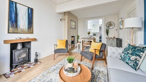 Ein Wohnzimmer mit Kamin, zwei Sesseln, einer Couch und einem Couchtisch, sowie einem großen abstrakten Gemälde.