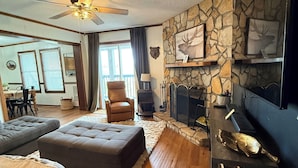 A living room with a fireplace, stone wall, and a television. - 2118  The Owl Cove! Level entry - Hot tub, sauna & more resort amenities (Beech Mountain)