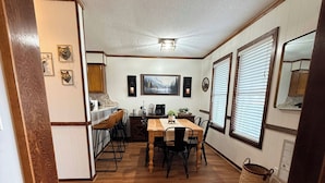 A dining area with a wooden table and chairs, a kitchen in the background, and a white rug on the floor. - 2118  The Owl Cove! Level entry - Hot tub, sauna & more resort amenities (Beech Mountain)
