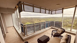 A balcony with wicker furniture and a view of a forested landscape.