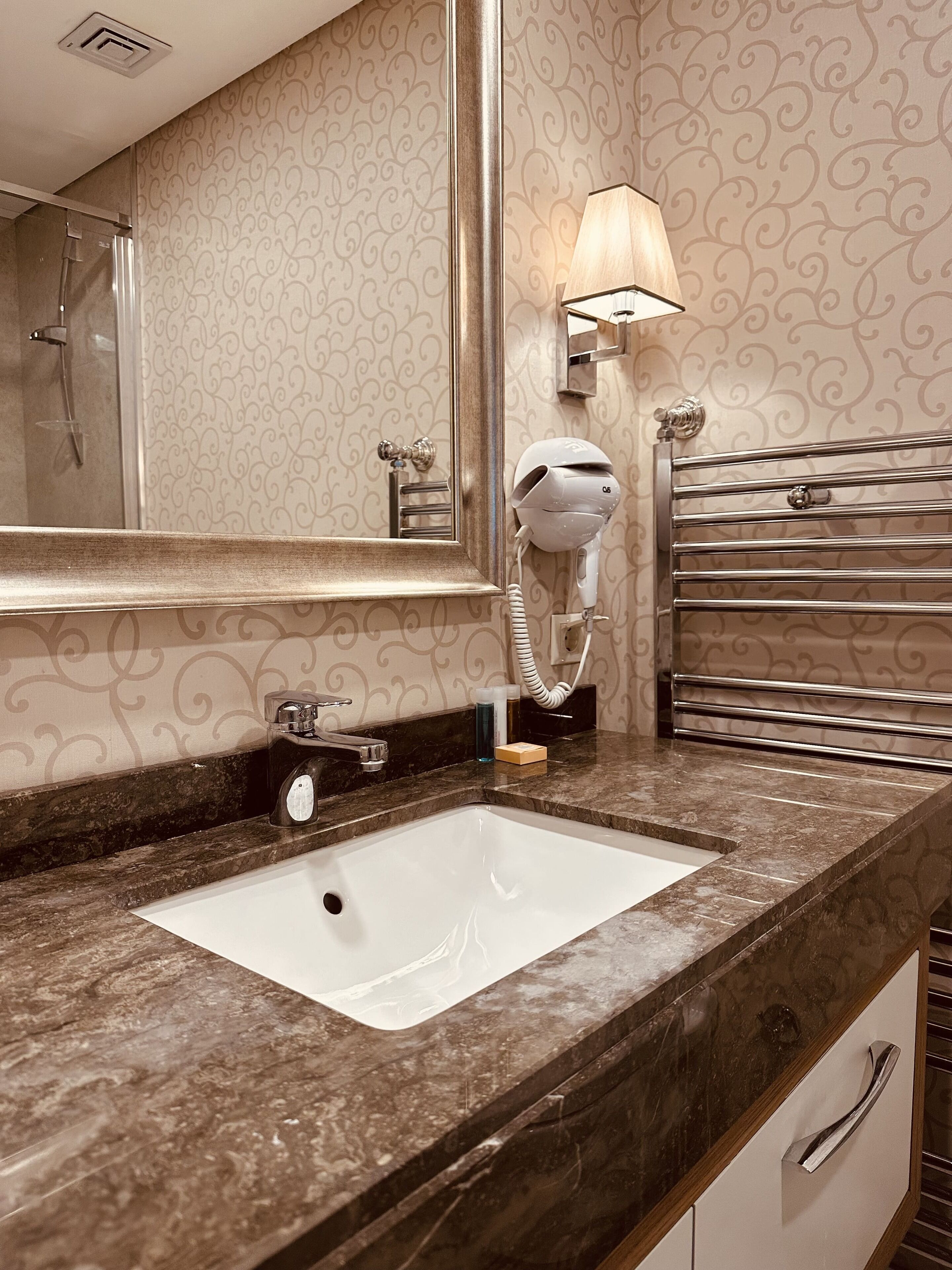 Un bagno con lavabo in marmo, portasciuga asciugamani, asciugacapelli e specchio.