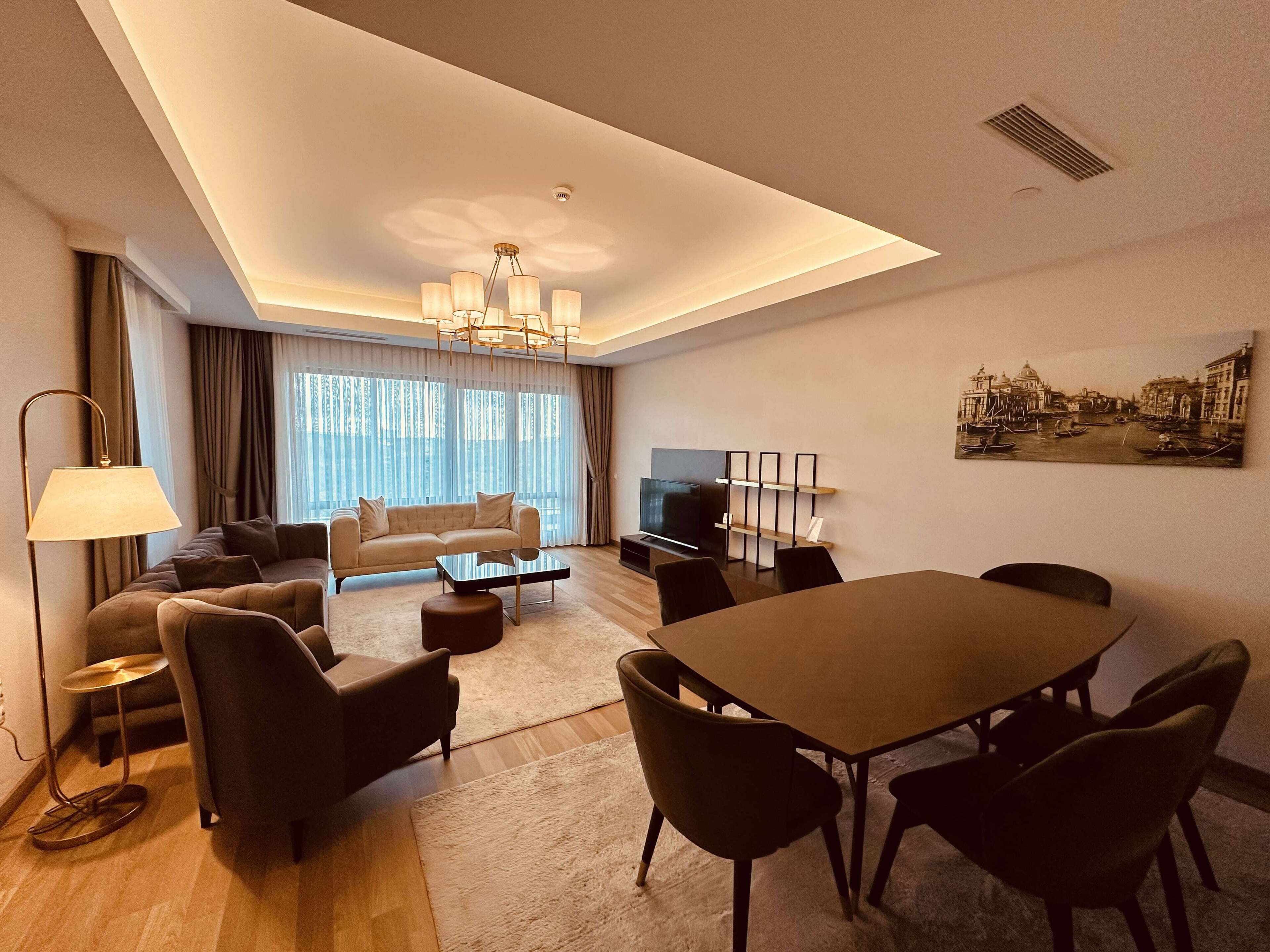 Ein modernes Wohnzimmer mit Sofa, Couchtisch, Fernseher und einem Essbereich mit Stühlen und Tisch.