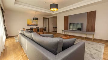 Uma sala de estar moderna com um sofá seccional cinza, uma mesa de centro de madeira e uma TV de tela plana fixada na parede.