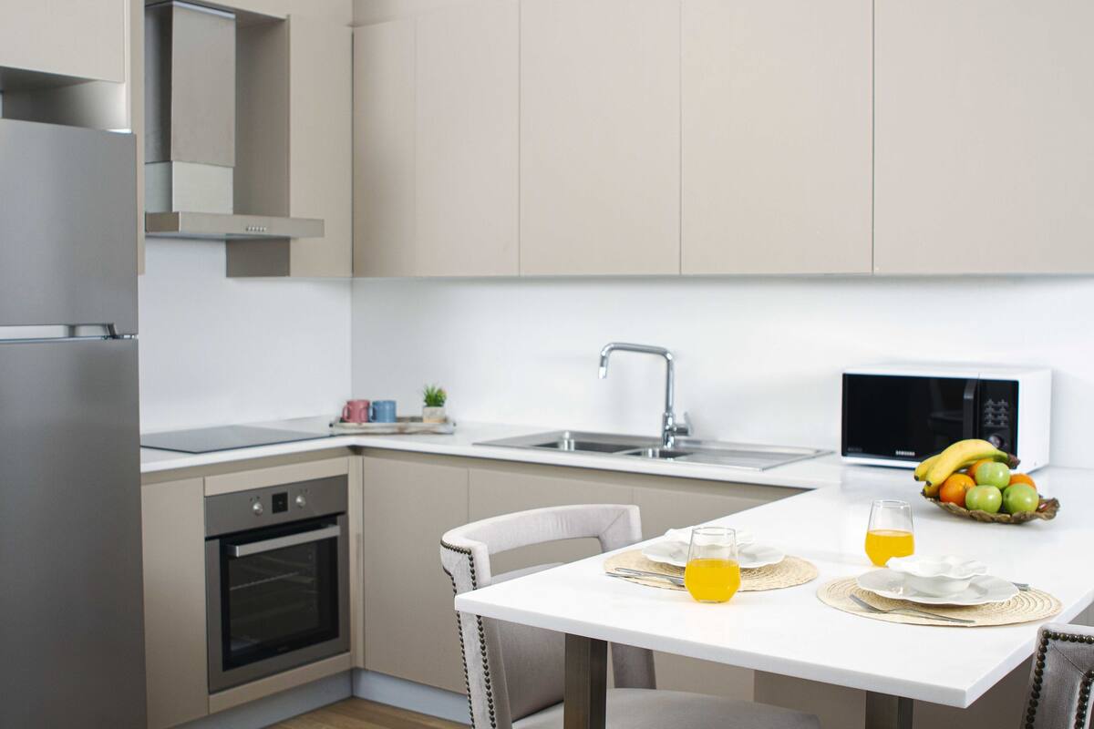 Une cuisine moderne dotée d’appareils électroménagers en acier inoxydable, d’un plan de travail blanc et d’un coin repas avec une table dressée pour deux personnes.