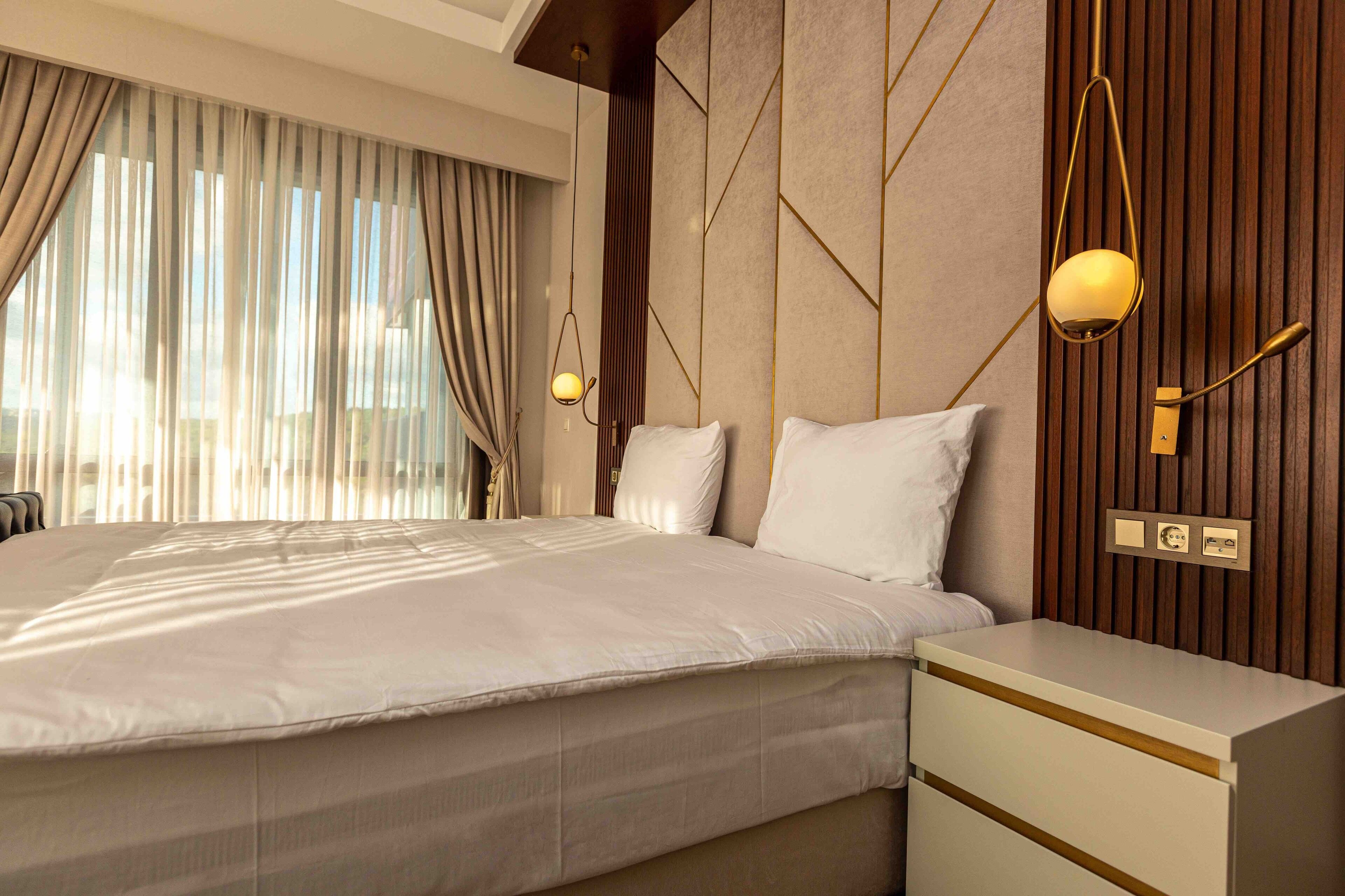 A modern hotel room with a large bed, bedside tables, and a wooden accent wall.