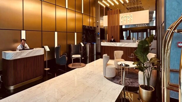 A modern hotel lobby with a reception desk, seating area, and a bar.