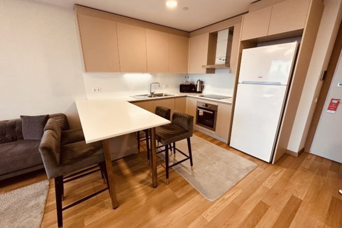 Una cocina compacta con cubierta blanca, dos taburetes de bar, un microondas, una estufa y un refrigerador.