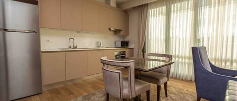 A modern kitchen with stainless steel appliances, a dining table with chairs, and a large window with sheer curtains.