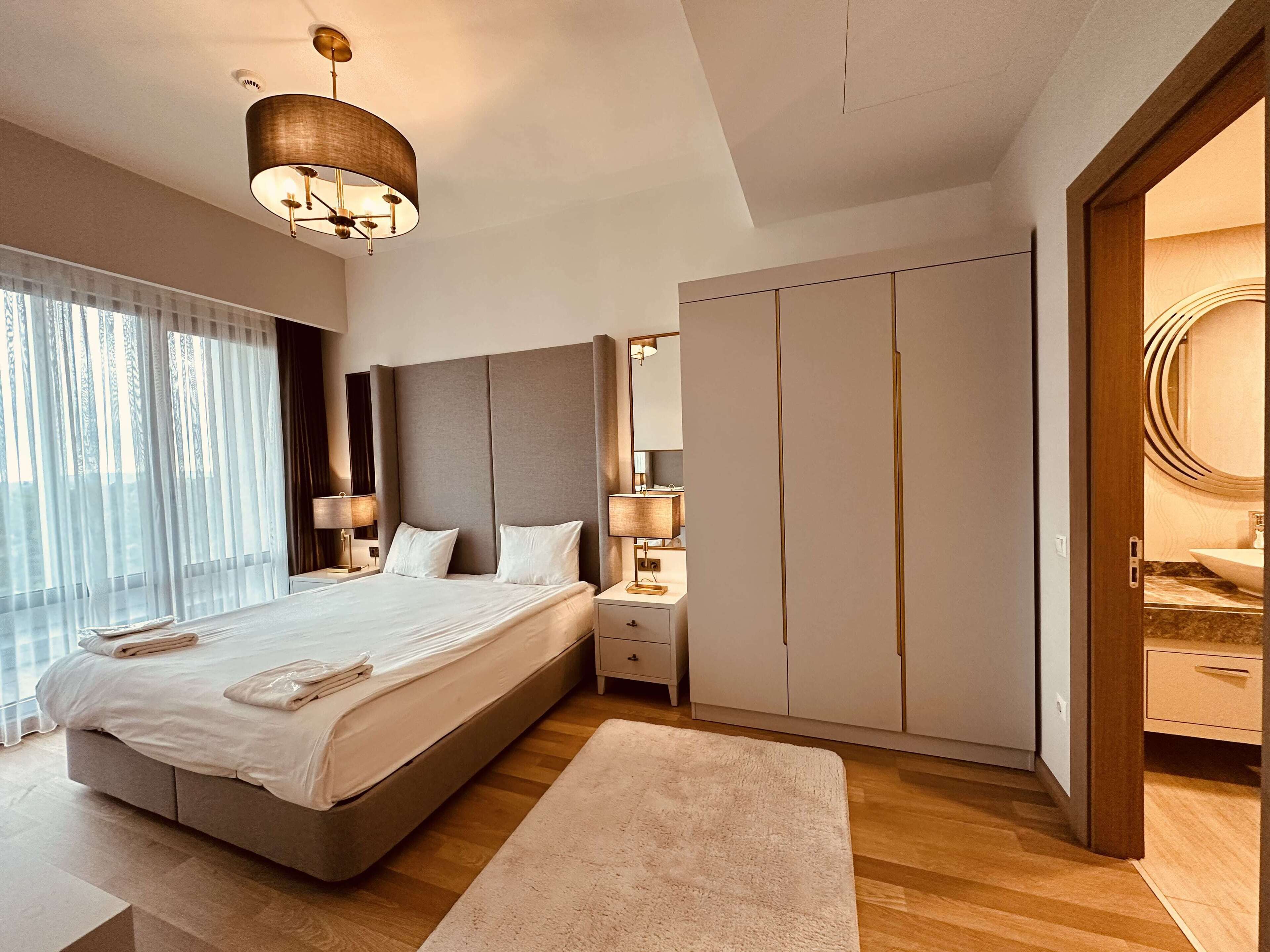 A modern bedroom with a large bed, bedside tables, a wardrobe, and a bathroom visible through an open door.