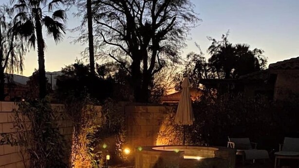 A swimming pool with a wooden deck, a stone wall, and a stone fountain. There are candles and a bottle of wine on the deck. - 🌟 VILLA SUNSTAR 🌟 Coachella & Stagecoach Next Door | 3 Bed (Indio)