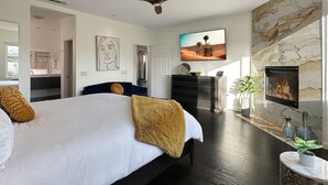 A modern bedroom with a large bed, a ceiling fan, a TV, a fireplace, and a view of the outdoors. - 🌟 VILLA SUNSTAR 🌟 Coachella & Stagecoach Next Door | 3 Bed (Indio)