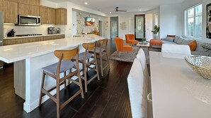 A modern kitchen with a central island, bar stools, and a dining area with orange chairs. - 🌟 VILLA SUNSTAR 🌟 Coachella & Stagecoach Next Door | 3 Bed (Indio)