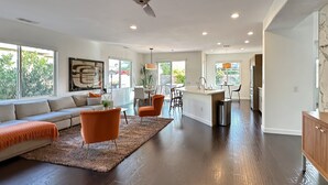 A spacious living area with a large sofa, orange chairs, and a kitchen island. - 🌟 VILLA SUNSTAR 🌟 Coachella & Stagecoach Next Door | 3 Bed (Indio)