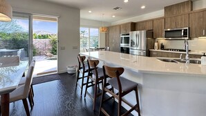 A modern kitchen with dark wood cabinets, stainless steel appliances, and a large island with bar stools. - 🌟 VILLA SUNSTAR 🌟 Coachella & Stagecoach Next Door | 3 Bed (Indio)