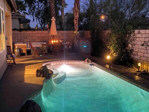 En swimmingpool med ett bubbelbad, omgiven av en mur av tegelsten och palmer.