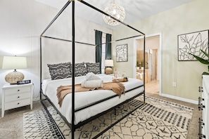A four-poster bed with a white and black patterned bedspread, a bedside table with a lamp, and a wall-mounted clock. - Disney Getaway w/ Private Pool, Hot Tub & Game Room (Kissimmee)