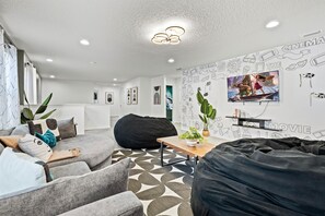A modern living room with a bean bag, grey sofas, a coffee table, and a wall with movie-themed decorations. - Disney Getaway w/ Private Pool, Hot Tub & Game Room (Kissimmee)