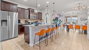 Cozinha moderna com ilha central, banquetas, eletrodomésticos de aço inoxidável e iluminação pendente.