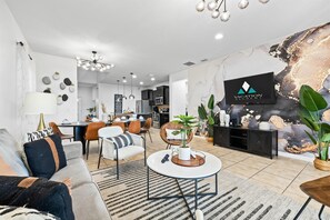 A modern living room with a sofa, coffee table, and dining area. - Disney Getaway w/ Private Pool, Hot Tub & Game Room (Kissimmee)