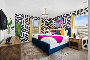 Ein modernes Schlafzimmer mit einem großen Bett, einer Kandelaberleuchte, einem farbenfrohen abstrakten Gemälde und Blick ins Freie.