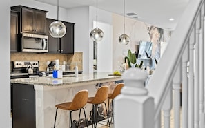 A modern kitchen with dark cabinets, stainless appliances, and a central island with bar stools. - Disney Getaway w/ Private Pool, Hot Tub & Game Room (Kissimmee)