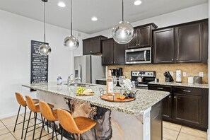 A modern kitchen with dark wood cabinets, stainless steel appliances, a granite countertop, and pendant lighting. - Disney Getaway w/ Private Pool, Hot Tub & Game Room (Kissimmee)