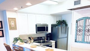 Una cocina moderna con armarios blancos, una isla central con taburetes de bar, electrodomésticos de acero inoxidable y un portón decorativo.
