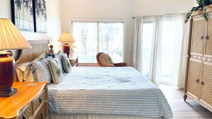 Un dormitorio con una cama grande, dos lámparas de noche, un aparador de madera y un ventanal con cortinas.