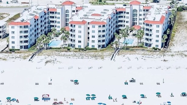 Un hotel frente a la playa con varias edificaciones, una playa de arena y sombrillas.