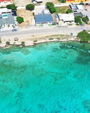 Vista aérea de una zona costera con edificios, una carretera y agua turquesa cristalina.