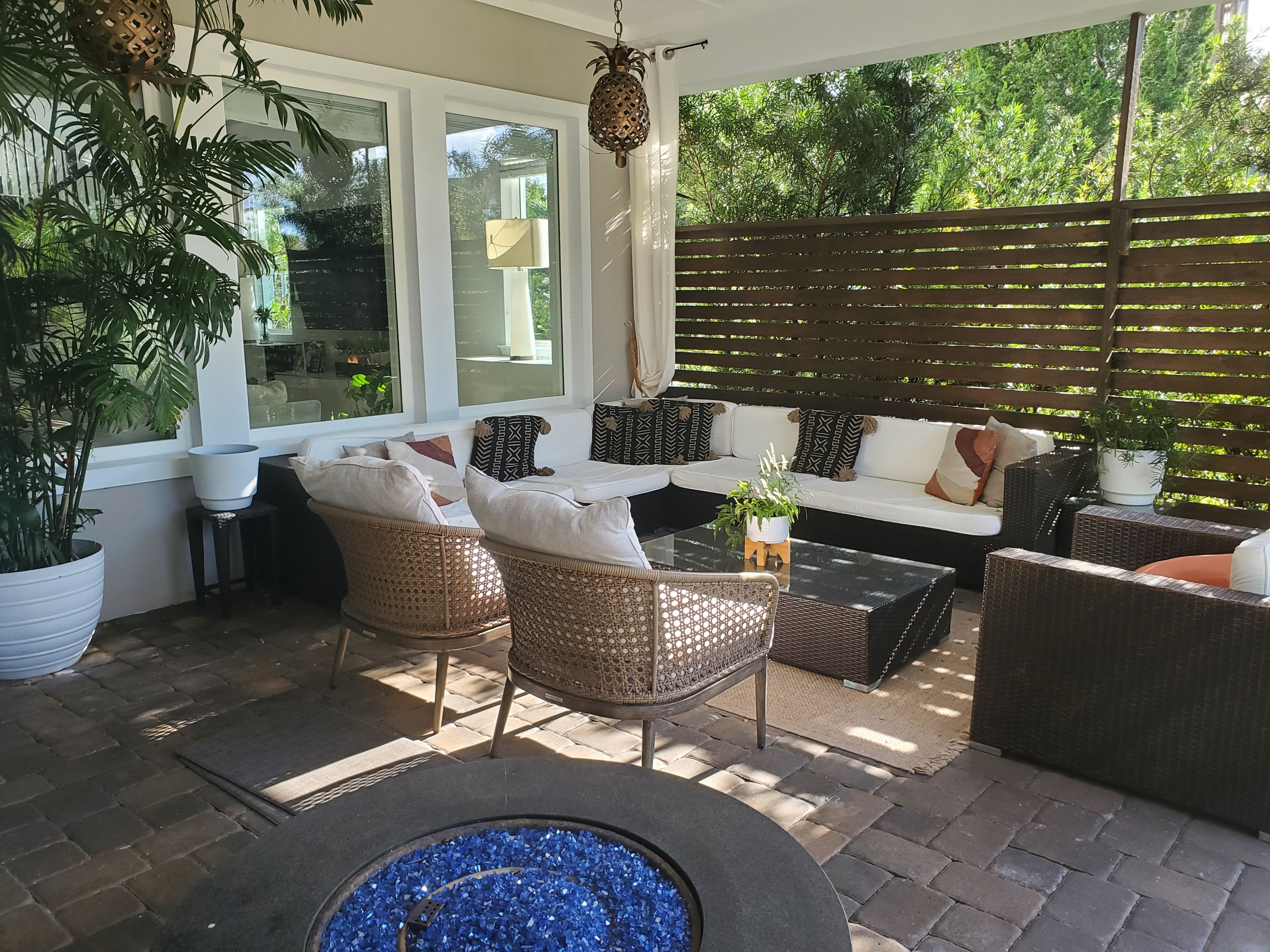 A covered patio area with wicker furniture, a glass-top coffee table, and a fire pit.