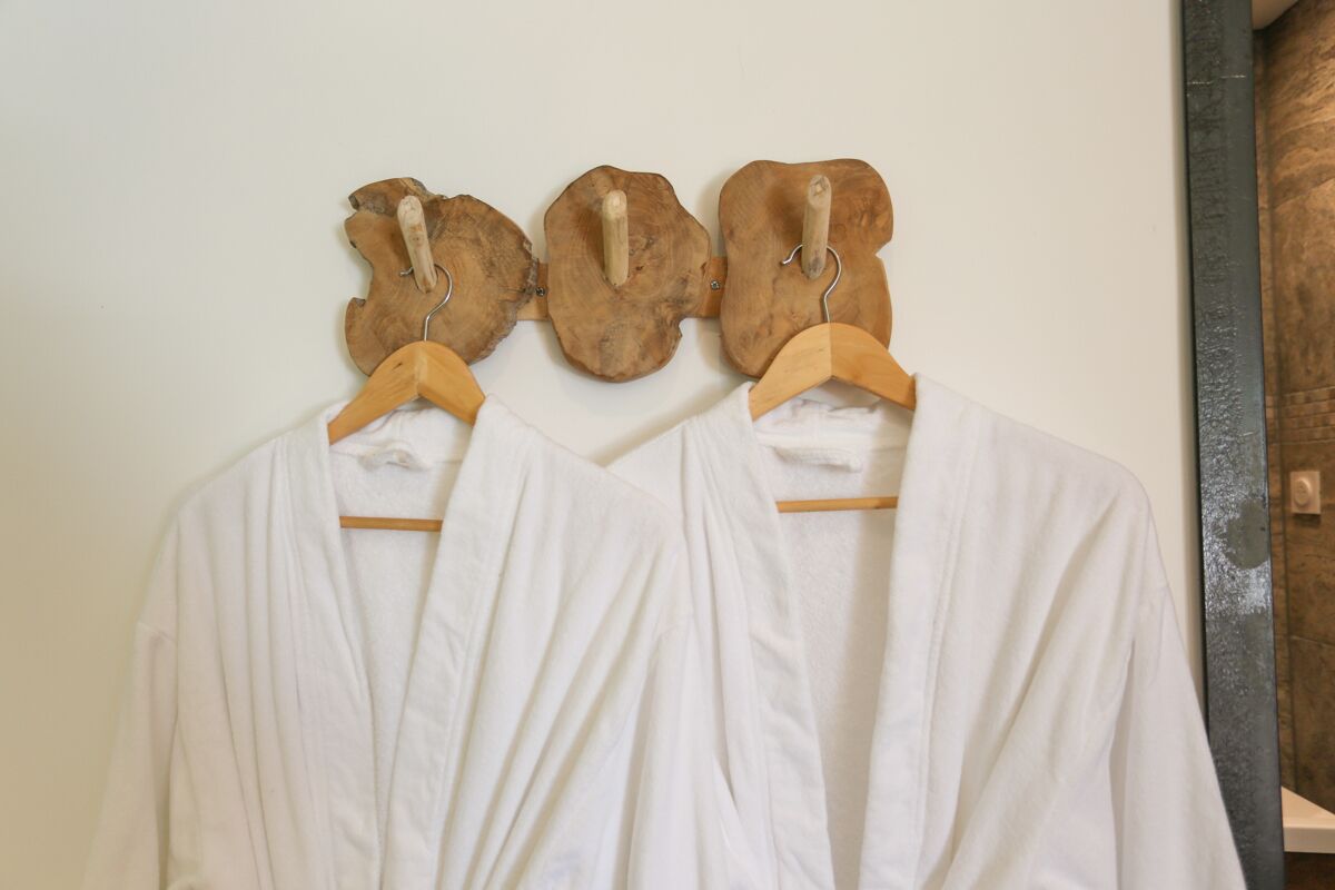 Two white robes hanging on wooden hangers against a wall.