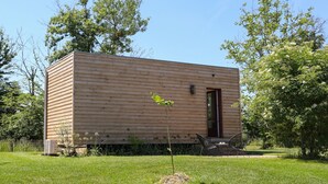 Een klein houten huisje met een deur, omringd door gras en bomen.