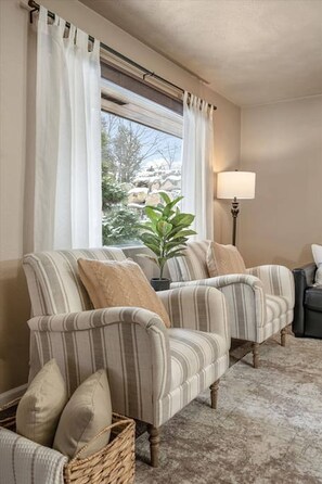 A room with two striped armchairs, a lamp, a potted plant, and a view of a snowy landscape through a window. - Spokane South Hill entertainer’s haven w/ theater, wine room & BBQ patio. (Spokane)