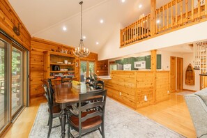 A wooden cabin interior with a dining area, kitchen, and a loft bedroom.
