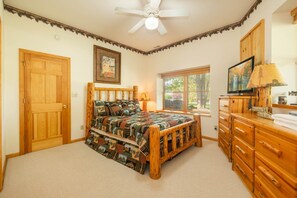 A bedroom with a wooden bed, a window, a television, and a wooden dresser.