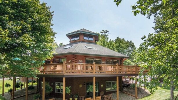 Une maison en bois à deux étages, dotée d’un balcon, d’une terrasse couverte et d’une cour clôturée.