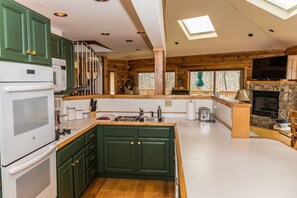 A modern kitchen with green cabinets, a central island, a stone fireplace, and a skylight.