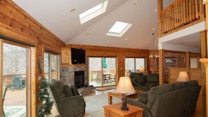 L’intérieur d’une cabane en rondins, avec une cheminée, des meubles en bois et de grandes fenêtres.