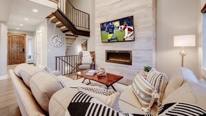 Un amplio salón con chimenea, un reloj grande y un televisor montado en la pared.