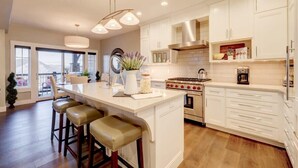 Una cocina moderna con armarios blancos, una isla central con taburetes, una estufa y un ventanal con vistas panorámicas.