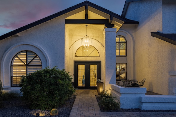A house with a well-lit entrance, a covered patio, and a brick pathway.
