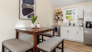Een moderne keuken met witte kastjes, een houten eettafel en een groot abstract schilderij.
