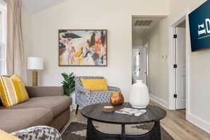 Una sala de estar con sofá, sillón, una mesita redonda y un cuadro en la pared.