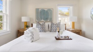 Een hotelkamer met een groot bed, twee nachtkastjes met lampen, een kunstwerk aan de muur en een raam met zonwering.