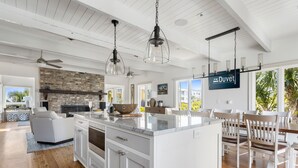 Una cocina amplia con una isla grande, armarios blancos y lámparas colgantes.