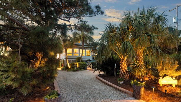 Un jardín bien cuidado con un sendero de grava que conduce a una casa. Hay un cartel con el nombre 'Captain Morgans'.